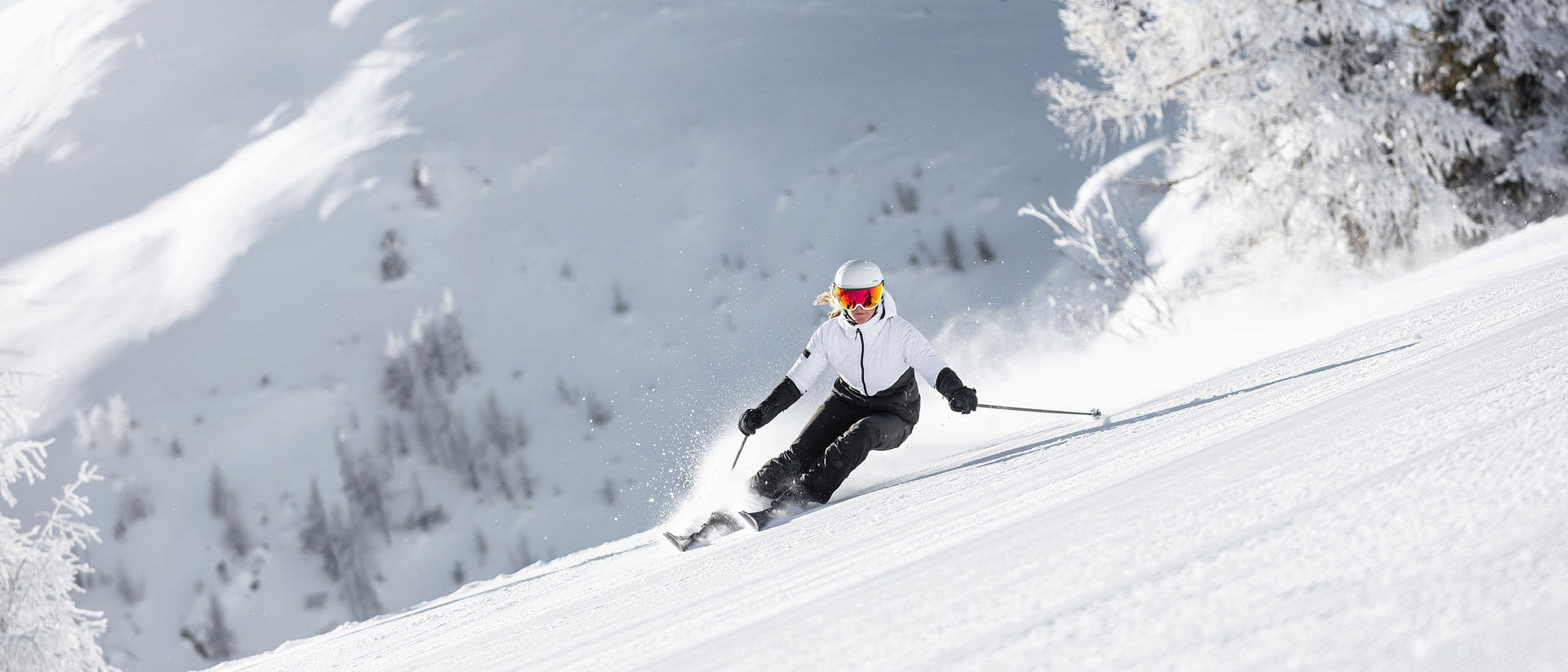 Skier descending a snowy slope with mountains and trees in the background wearing an Atomic Savor visor ski helmet