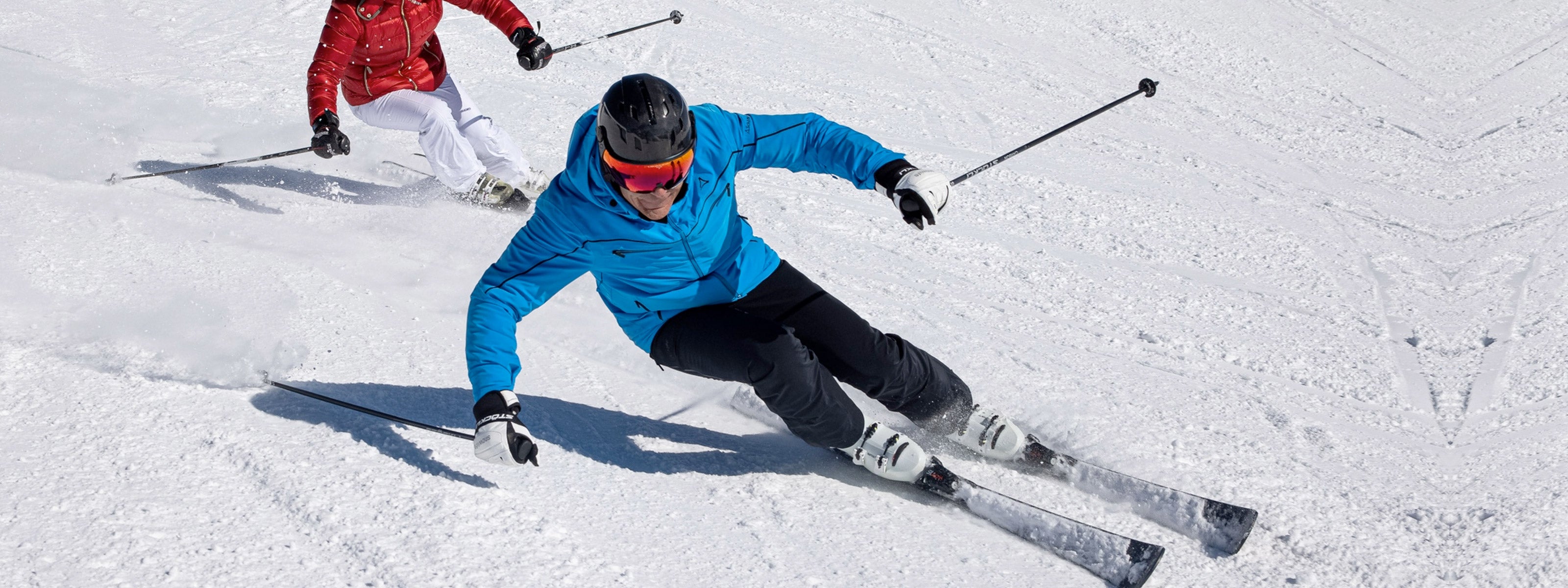 Person skiing downhill on a snowy slope with another skier in the background with black carbon visor ski helmet