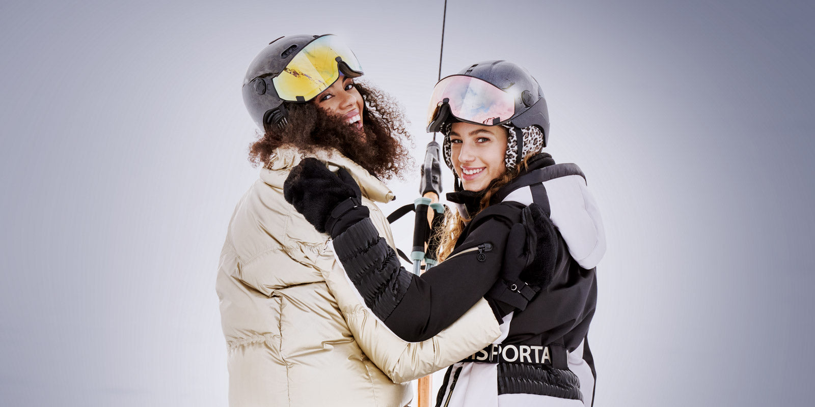 Two women on t-bar ski chairlift wearing Coya visor ski helmets from CP SPorts
