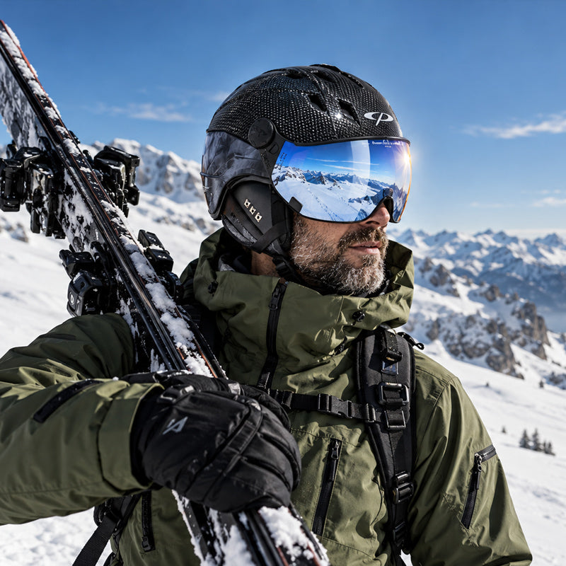 man wearing a black carbon visor ski helmet with skis over his shoulder in the mountains